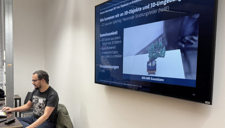 Foto des Workshops, Dominic Fehling, sitzend an einem Computer, die Präsentation zum Workshop im Hintergrund auf einem großen Bildschirm sichtbar.